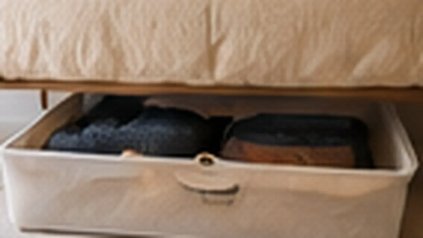 A shallow under-bed storage box pulled out slightly, holding folded off-season items, tucked beneath a neatly made bed